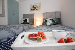A bed with patterned bedding, a tray with a tart, strawberries, and a cup of coffee.