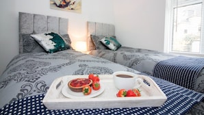 Una cama bien hecha con ropa de cama estampada, una bandeja con un pastel, fresas y una taza de café.
