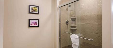 A glass-enclosed shower with a towel rack, beige walls, and two framed pictures.