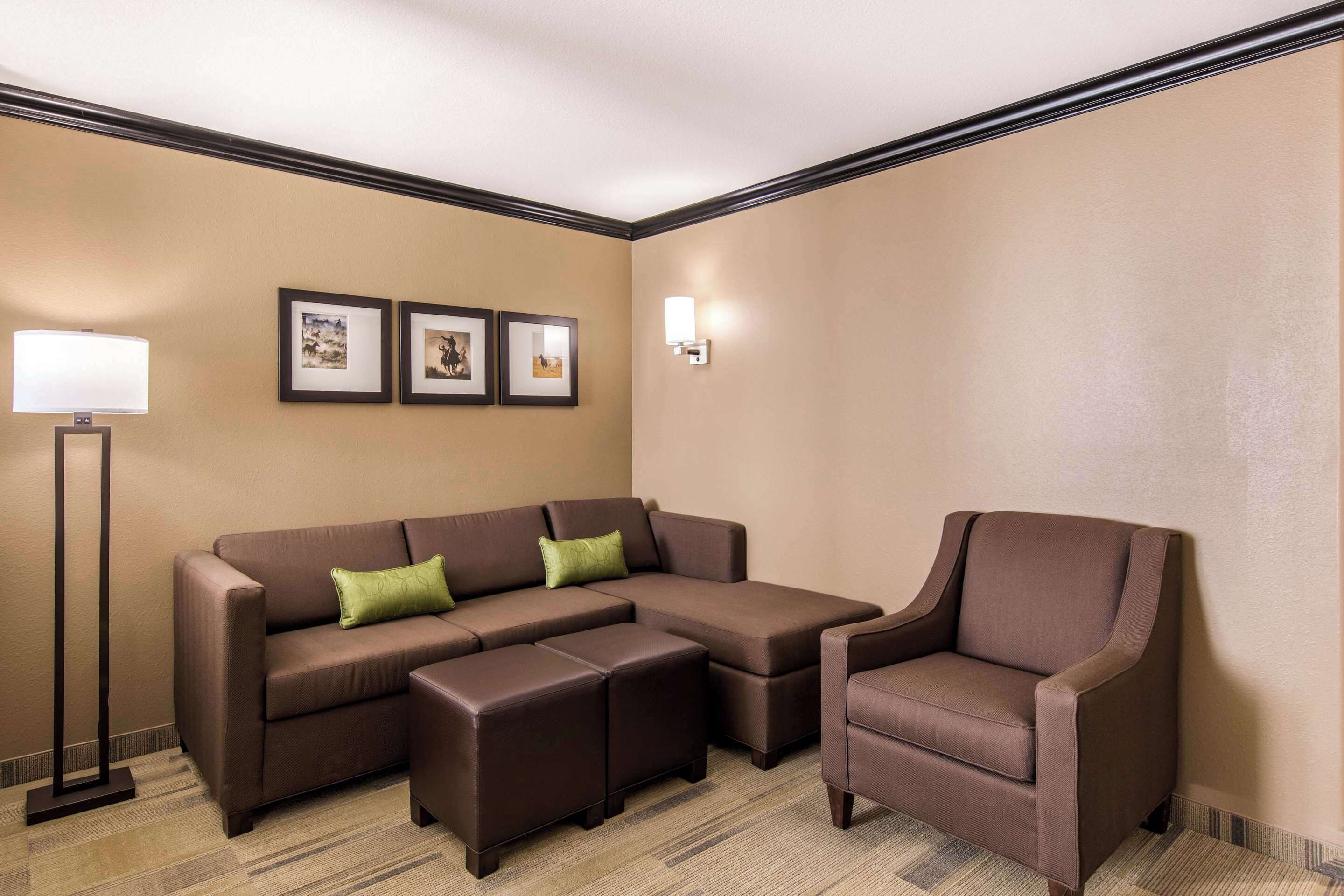 A room with a sectional sofa, a chair, a floor lamp, and framed pictures on the wall.