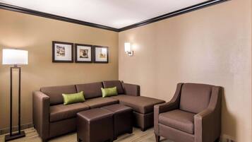 A room with a sectional sofa, a chair, a floor lamp, and framed pictures on the wall.