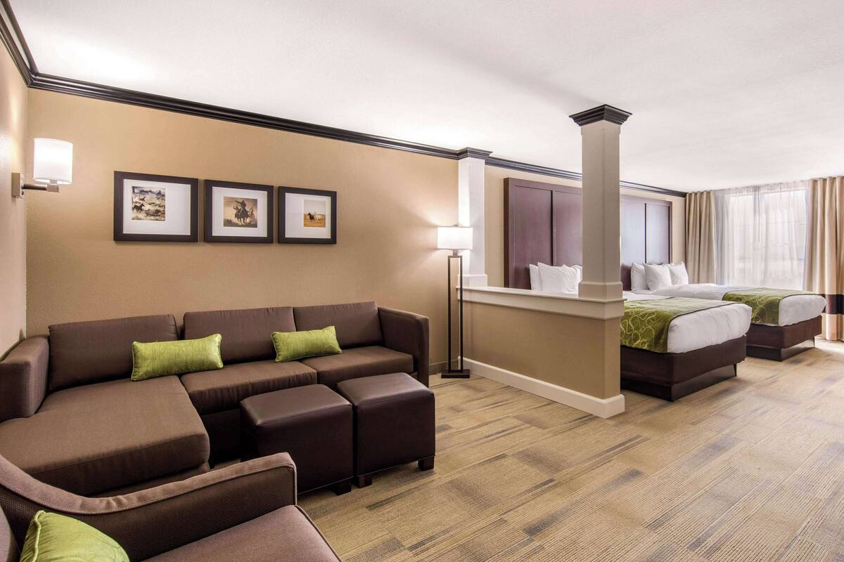 A hotel room with a sofa, ottoman, two beds, a desk, and framed pictures on the wall.