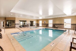 Una amplia piscina interior con carriles claramente delimitados, una zona de descanso con sillas y vistas al exterior a través de grandes ventanales.