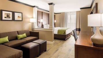 Habitación de hotel con sofá, reposapiés, cama y escritorio con lámpara.
