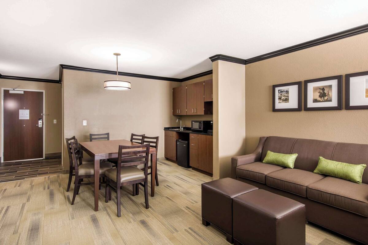 A hotel room with a dining table, chairs, a sofa, a kitchenette, and framed pictures on the wall.