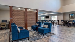 Un hall espacioso con sillones azules, una separadora de madera y un área de comedor con mesas y sillas.