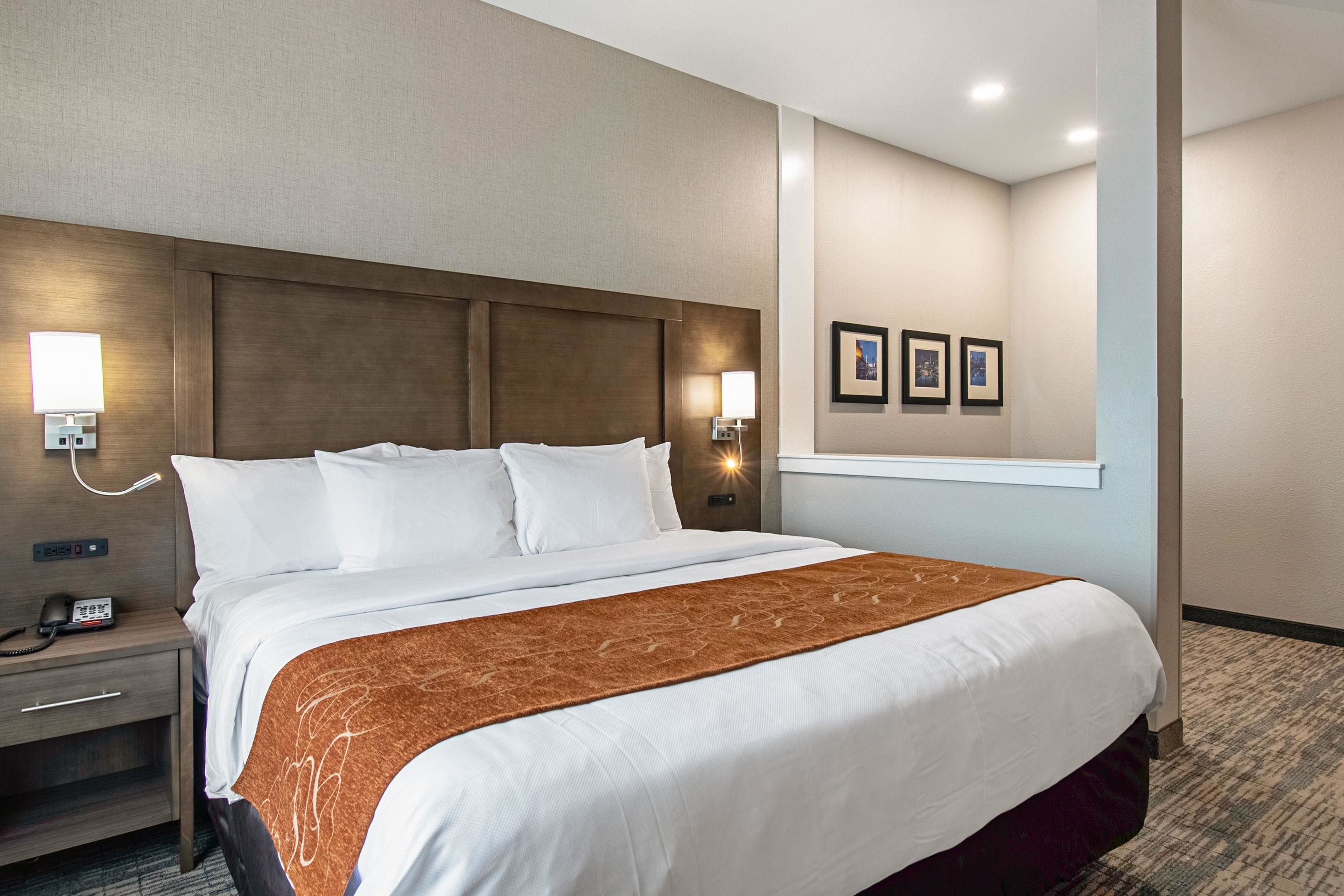 Una habitación de hotel con una cama grande, una mesita de noche con teléfono, luces empotradas y cuadros en la pared.