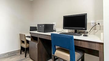 A hotel room with a desk, a computer, a monitor, and a chair.