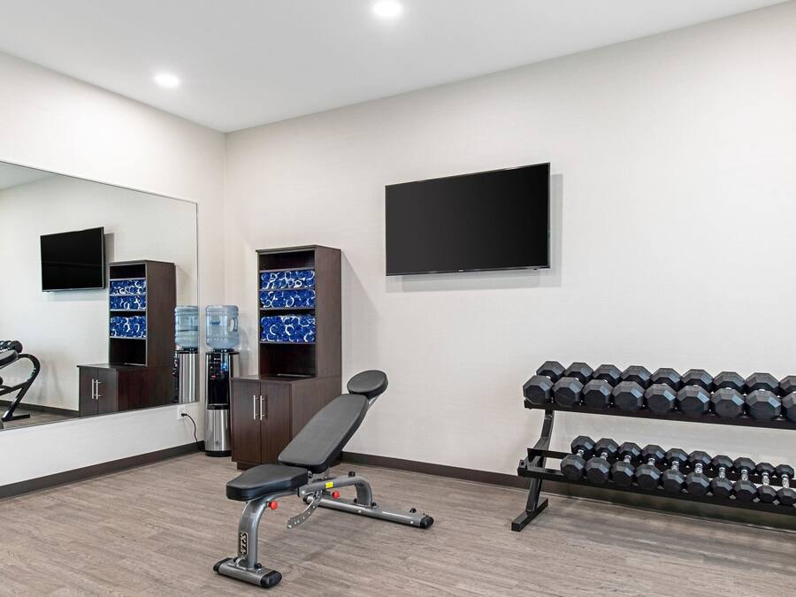 Un gimnasio con equipo de ejercicio, dispensadores de agua y una televisión en la pared.