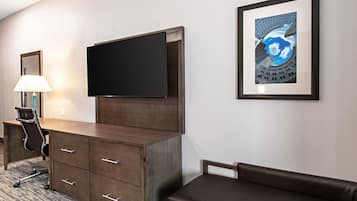 Een hotelkamer met een houten bureau, een flatscreen televisie, een ingelijst kunstwerk aan de muur en een bruine leren bank.
