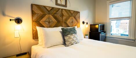 A neatly made bed with a wooden headboard, two bedside lamps, and a mounted deer skull.