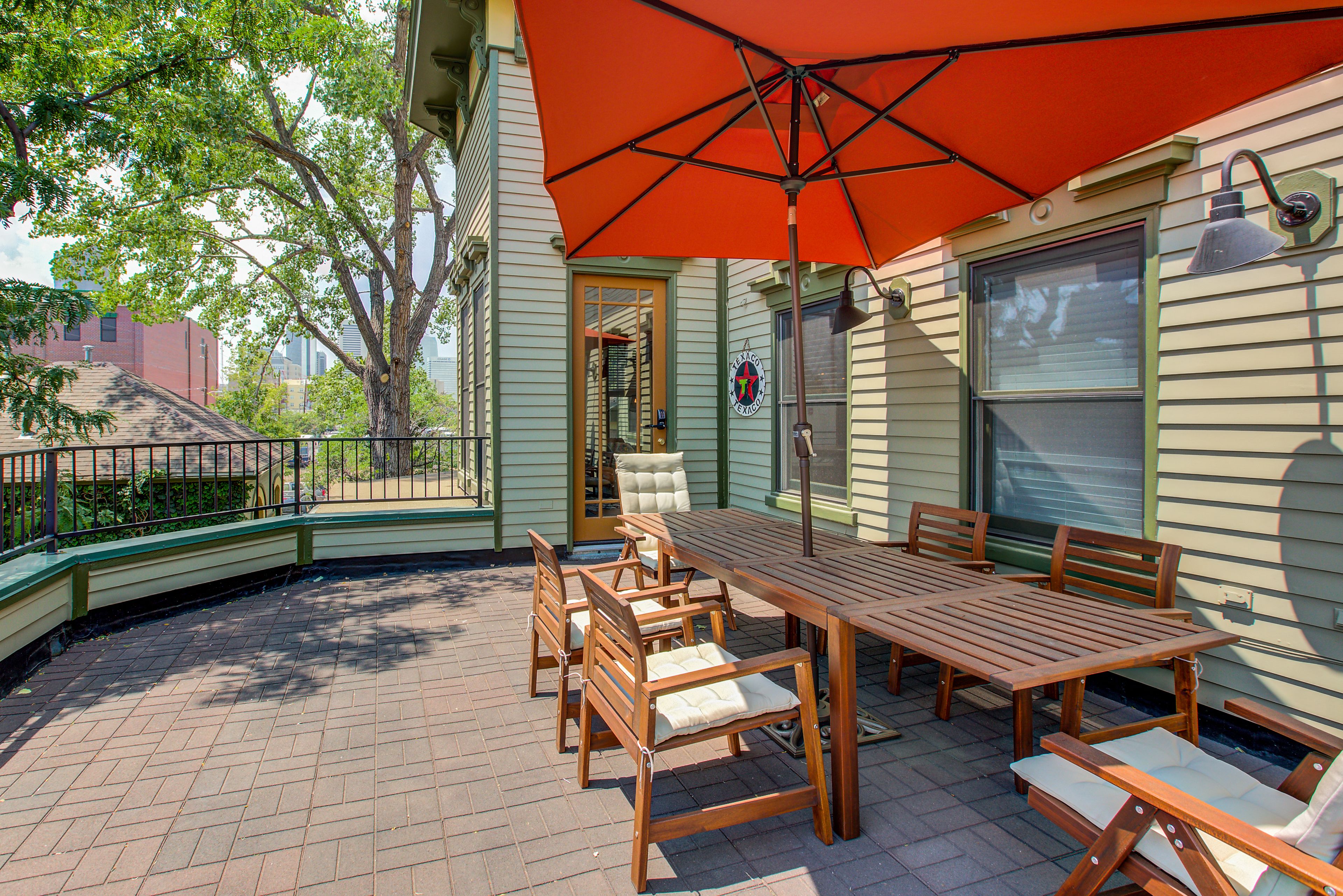 A wooden patio with a table and chairs, an orange umbrella, and a brick floor.