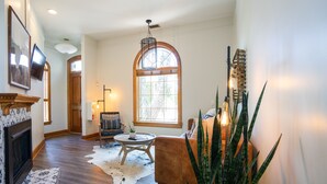 A spacious living room with hardwood floors, a fireplace, a large window, and a cozy seating area. - The Curtis Park Club (Denver)