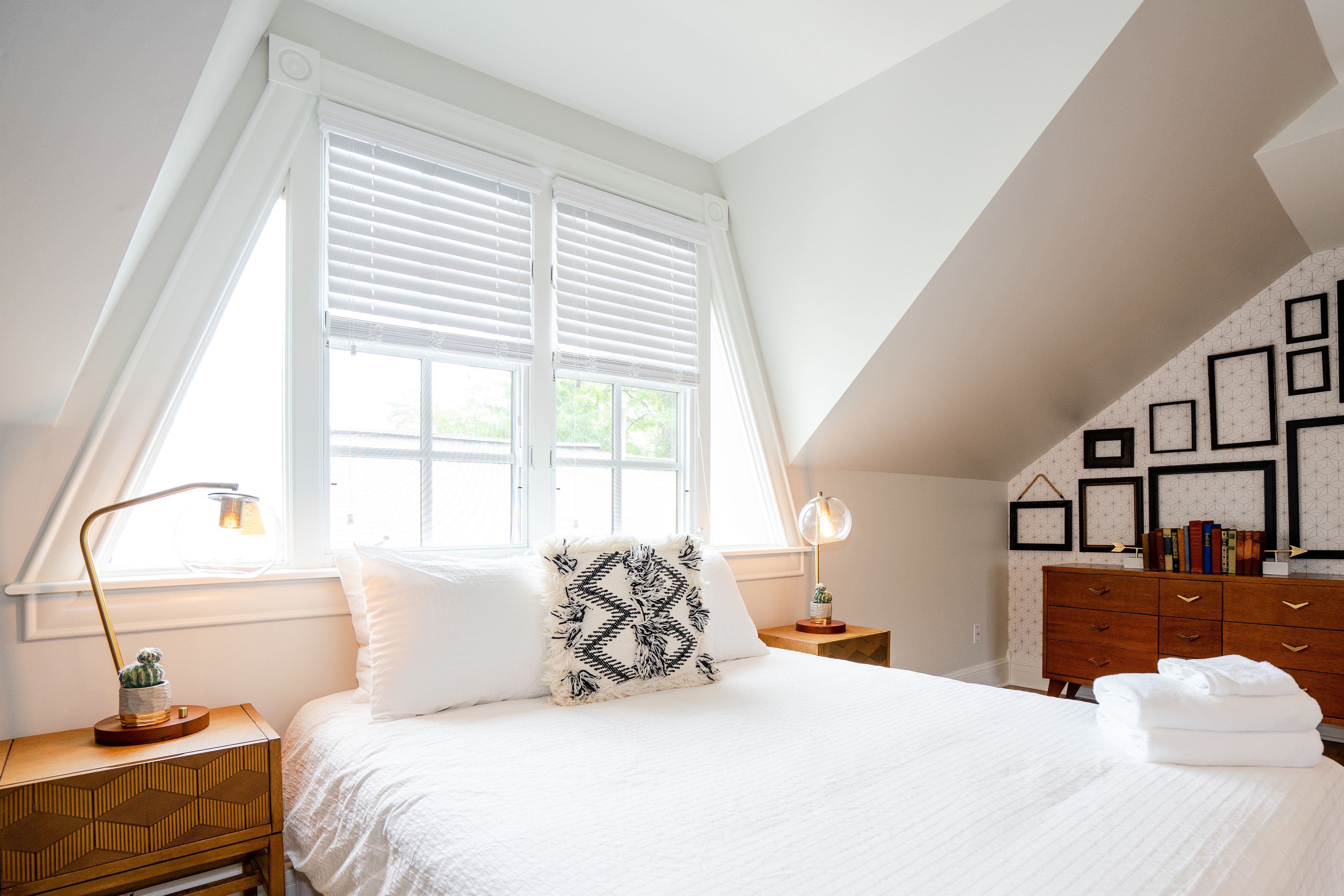 A bedroom with a bed, two bedside tables, a dresser, and a window with blinds.
