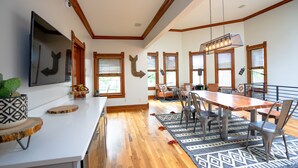 A modern kitchen with wooden floors, a dining area with a large table and chairs, and large windows with blinds. - The Curtis Park Club (Denver)