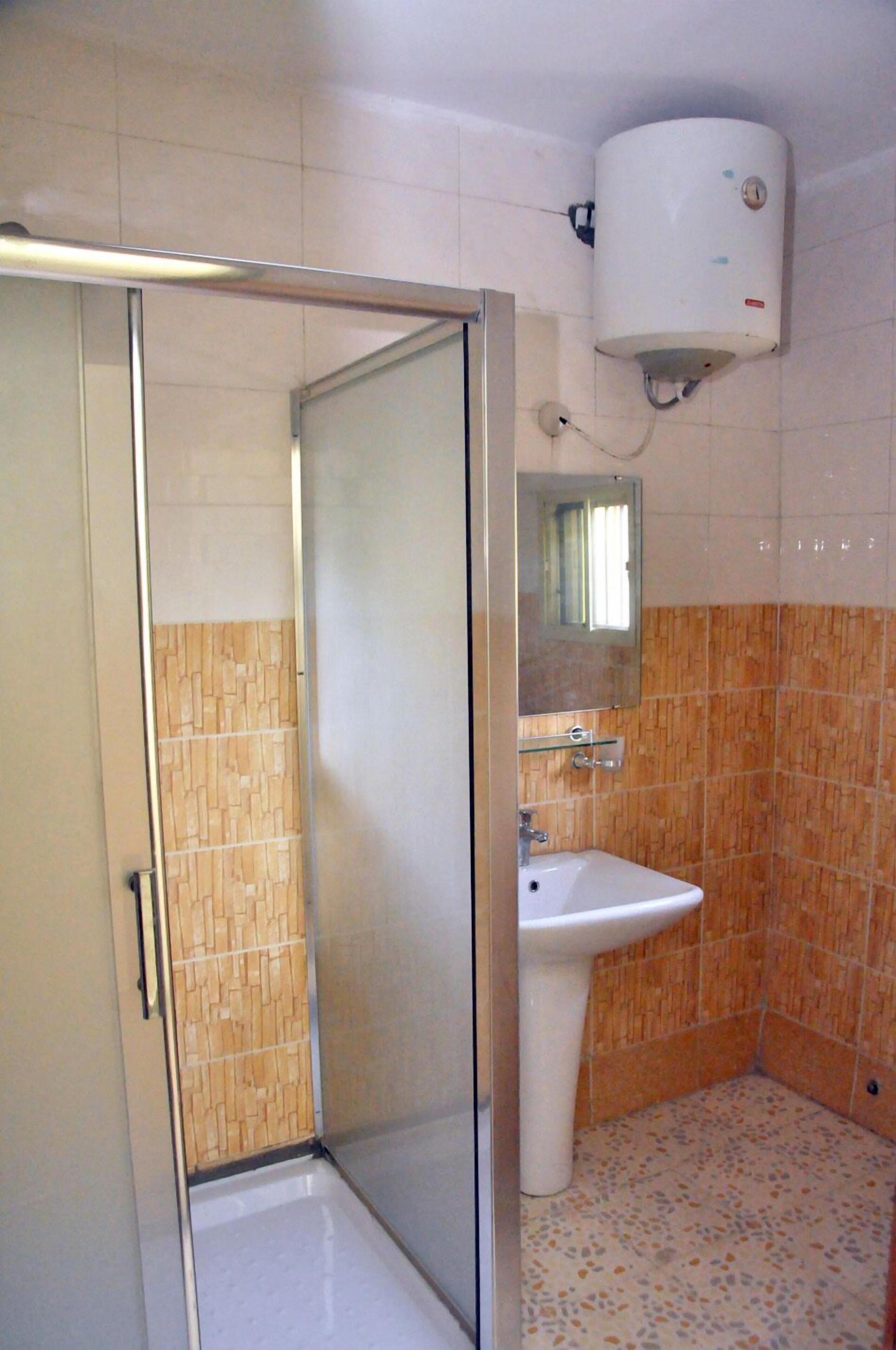 Een badkamer met een douche, een wastafel, een spiegel en een boiler.