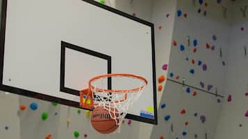 A basketball hoop with a mounted basketball, set against a wall with colorful climbing holds.