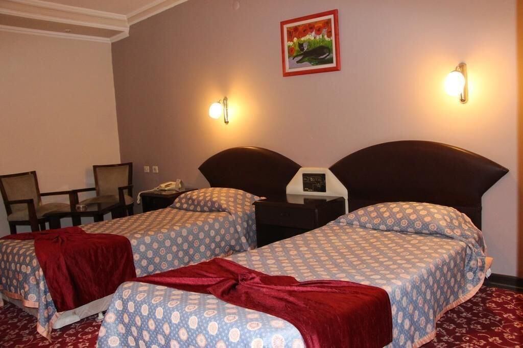 A hotel room with two beds, a desk, a chair, and a nightstand with a phone.