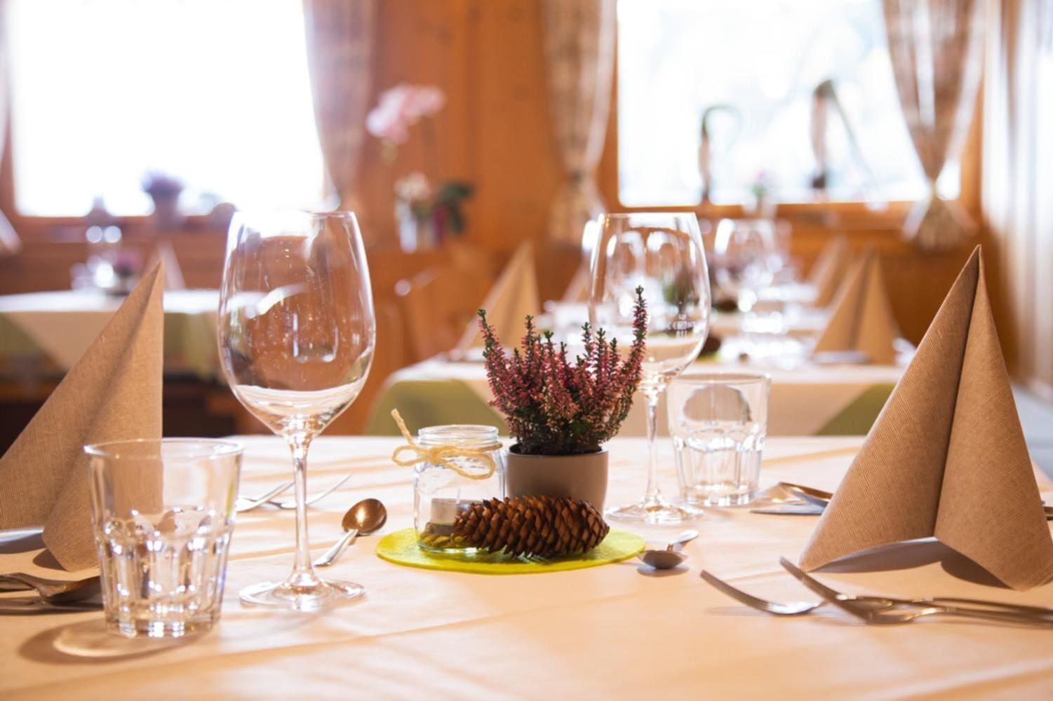 A dining table set with wine glasses, water glasses, and cutlery, with a small plant centerpiece.