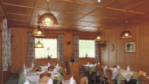 A wooden dining area with tables set for dining, large hanging lamps, and curtains on the windows. - Bergerhof (Sarentino)