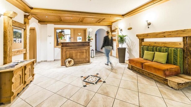 A lobby with a wooden reception desk, a sofa with cushions, and a tiled floor. - Bergerhof (Sarentino)