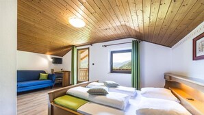 A bedroom with a wooden ceiling, a bed with white linens, a blue sofa, and a window with a view of the outdoors. - Bergerhof (Sarentino)