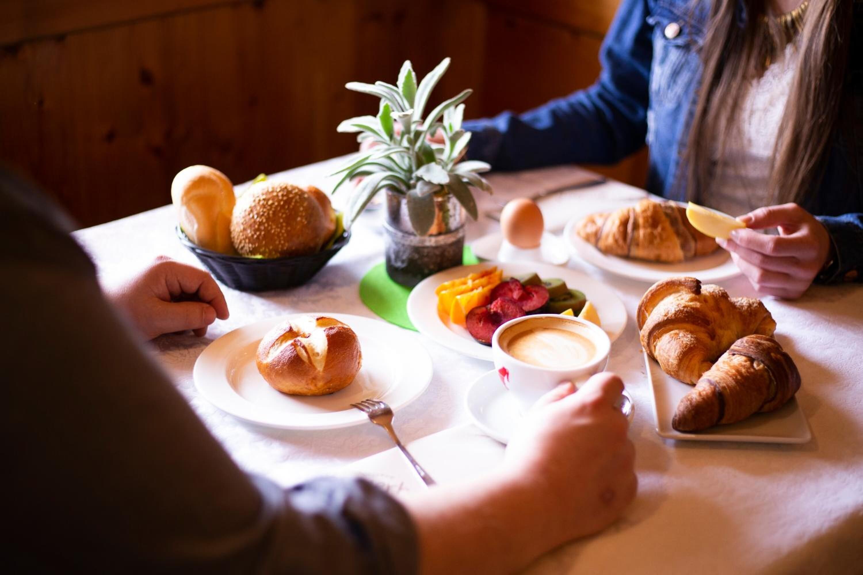 A dining table with various food items including croissants, a bowl of bread, and a small plant.