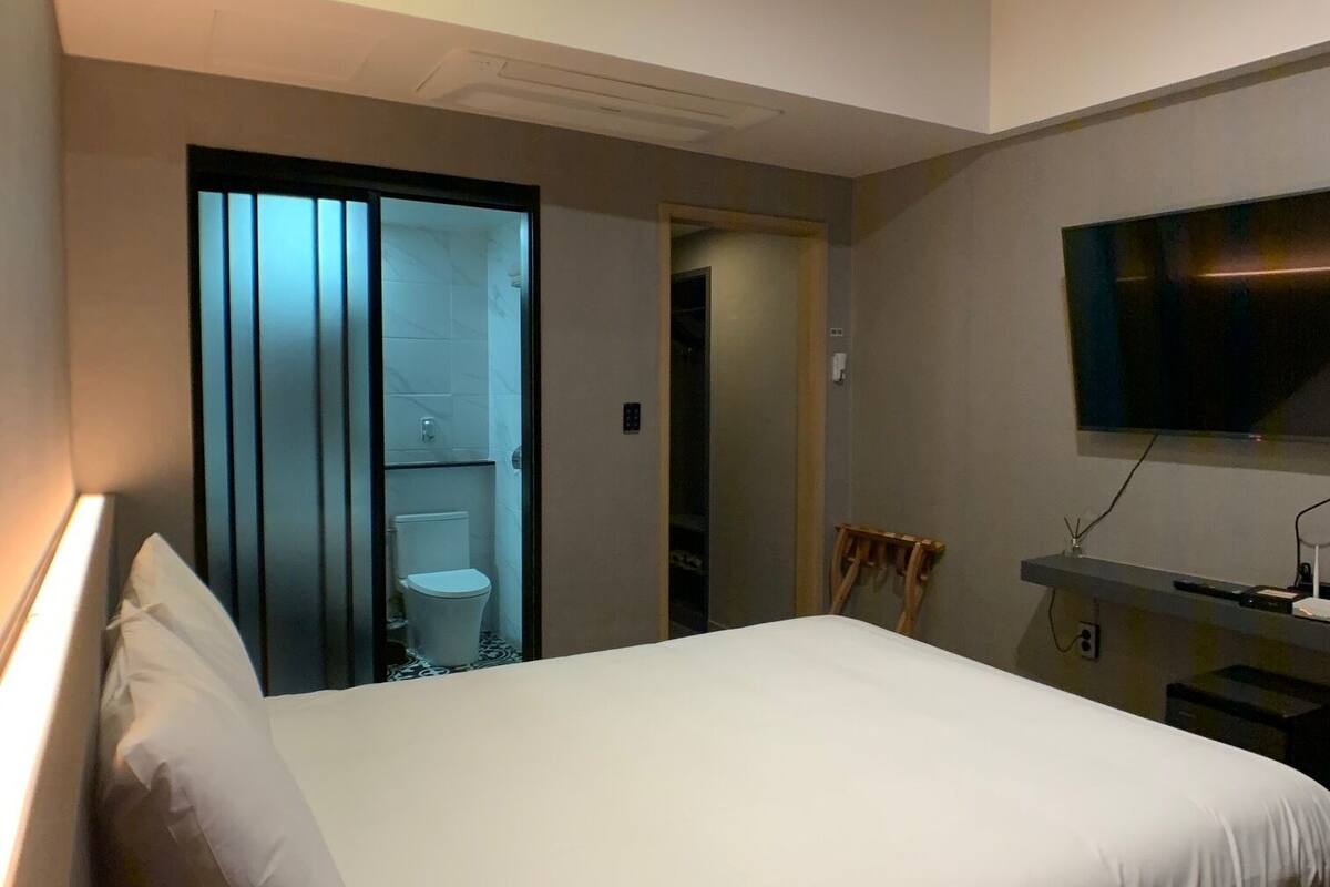 Et hotelværelse med en seng, et fjernsyn og et badeværelse, der kan ses gennem en skydedør.