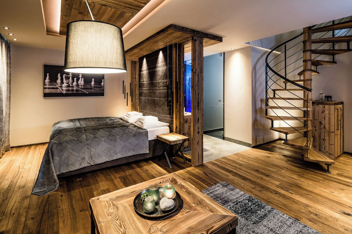 Ein modernes Schlafzimmer mit einem großen Bett, Holzboden, einer Wendeltreppe und einem kleinen Nachttisch mit einer Schale dekorativer Gegenstände.
