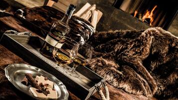 A cozy setting with a fur-covered couch, a tray with a bottle and glasses, and a plate with chocolate and nuts.