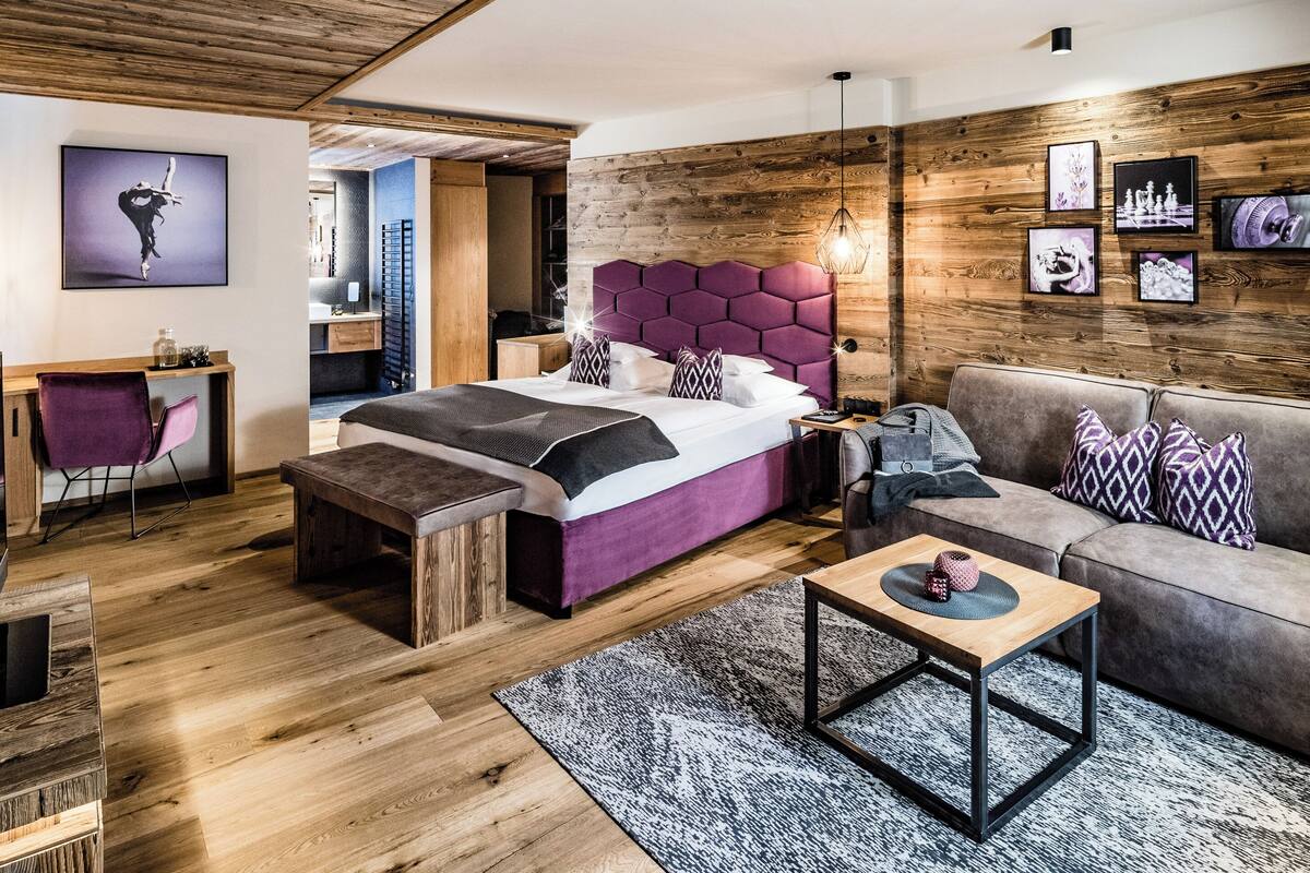 Ein modernes Schlafzimmer mit Holzboden, einem großen Bett mit violettem Kopfteil, einem grauen Sofa und einem kleinen Tisch mit Teppich.