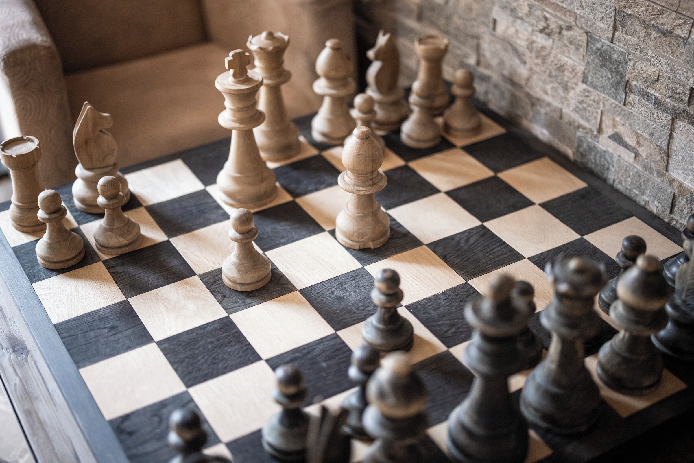 A chessboard with pieces in a room with stone walls and a patterned sofa.