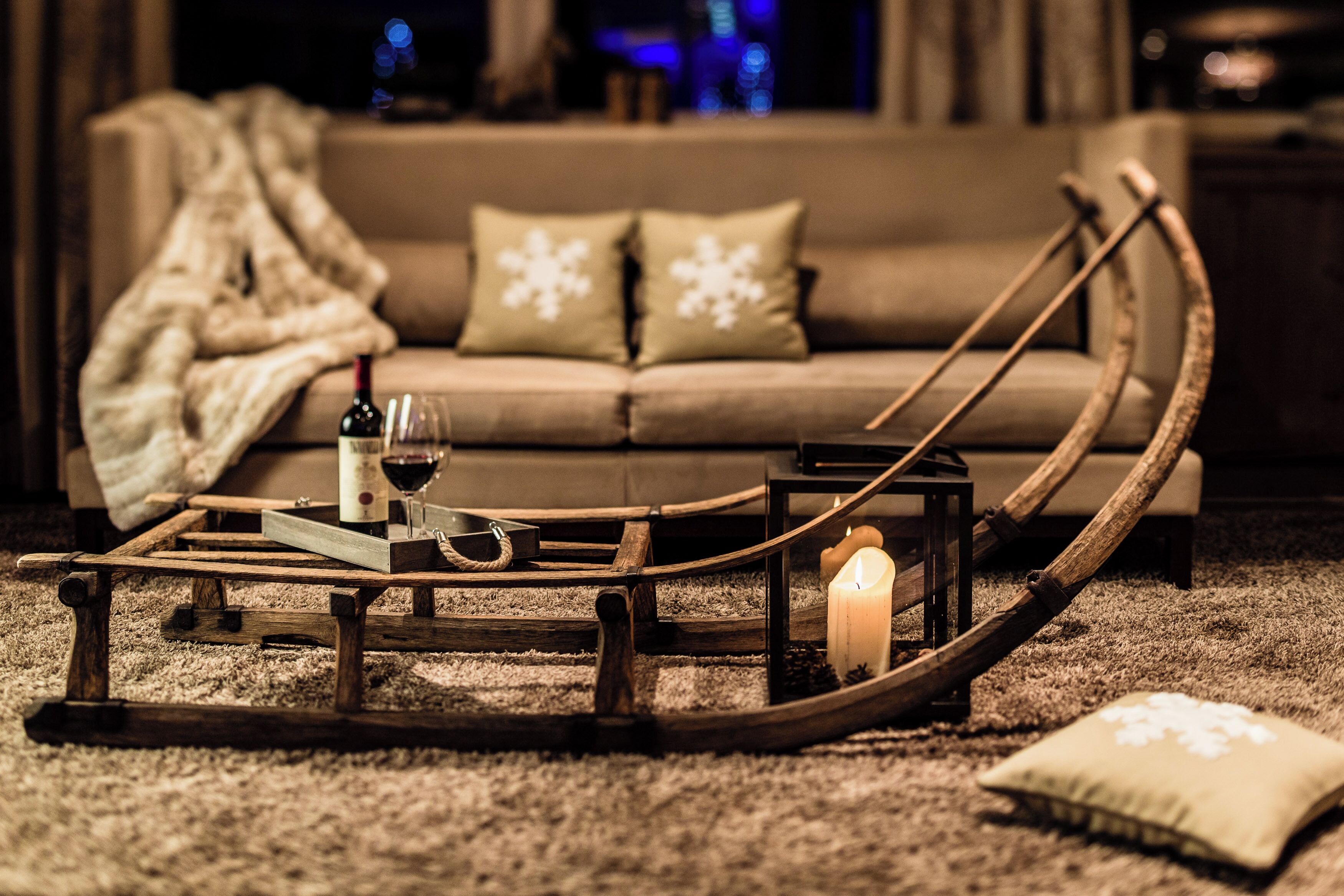 A cozy living room with a sofa, a wooden boat-shaped coffee table, a candle, and a bottle of wine.