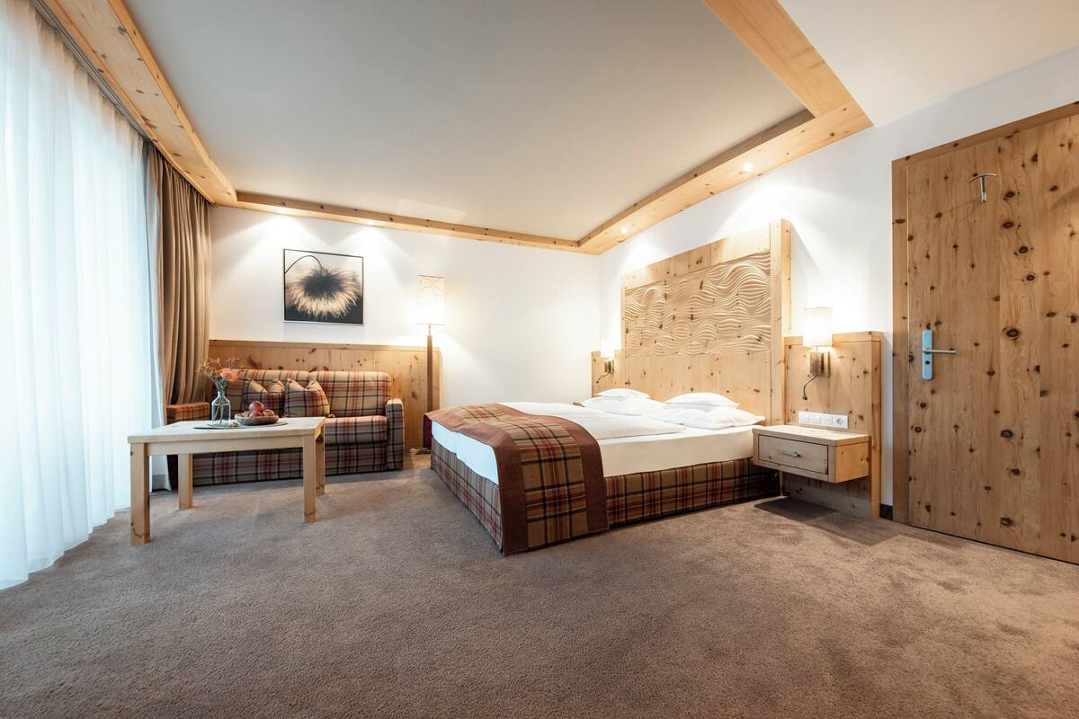 Ein modernes Hotelzimmer mit einem großen Bett, einem Holzkopfende, einem Nachttisch, einem Schreibtisch und einer Sitzecke.