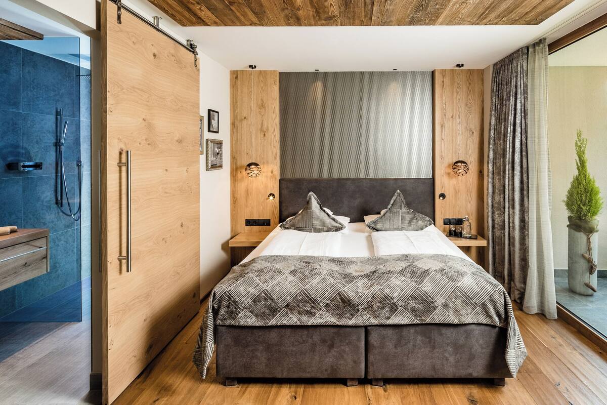 Ein modernes Schlafzimmer mit einem großen Bett, Holzwandverkleidung und Blick ins Badezimmer.