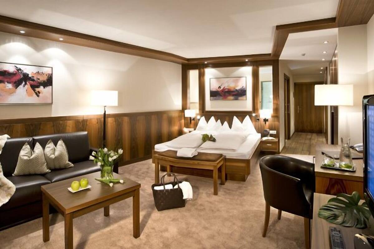 Ein Hotelzimmer mit einer Couch, einem Bett, einem Schreibtisch, einem Fernseher und Kunstwerken an den Wänden.