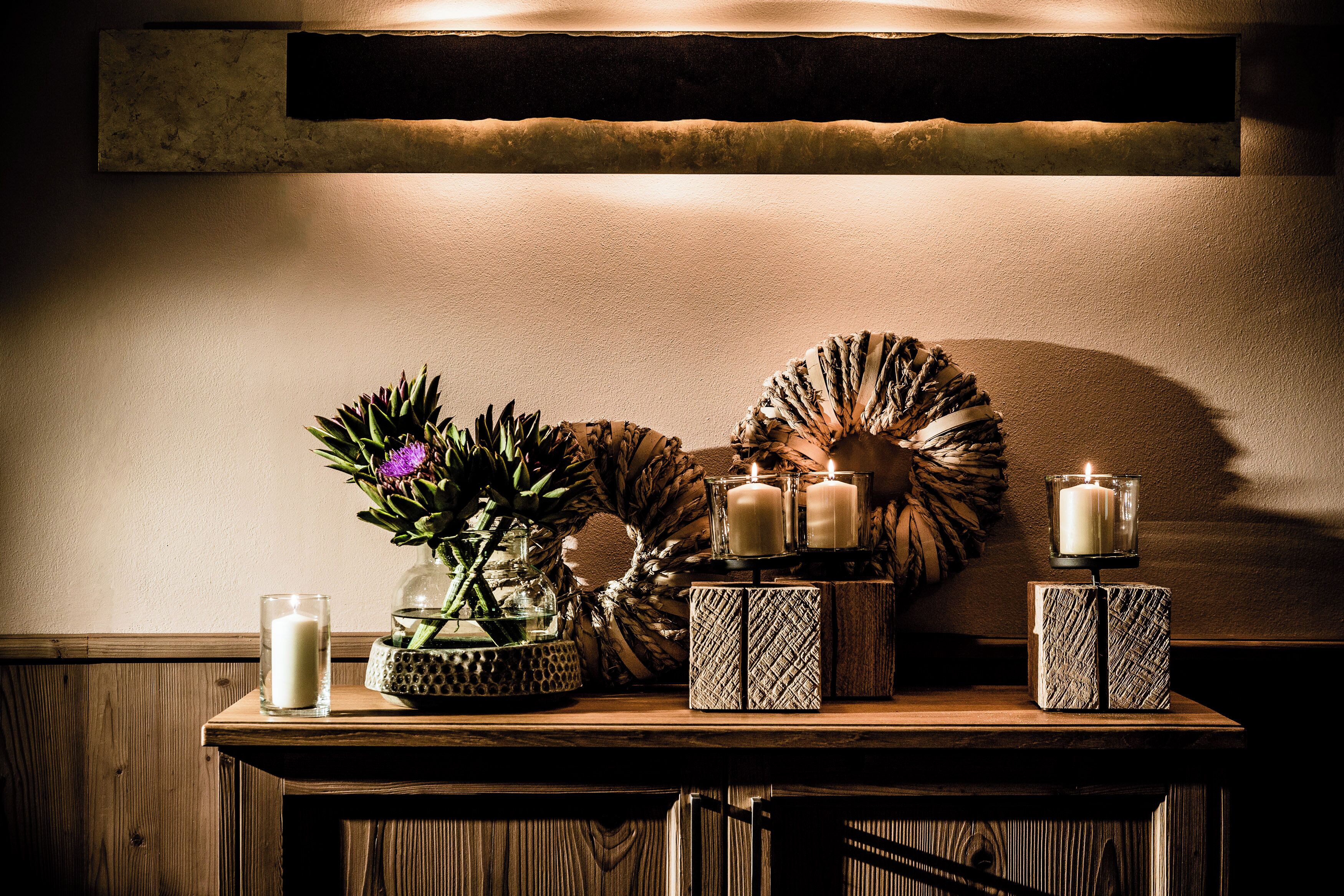 Una mesa de madera con velas, un florero de vidrio con flores y objetos decorativos.
