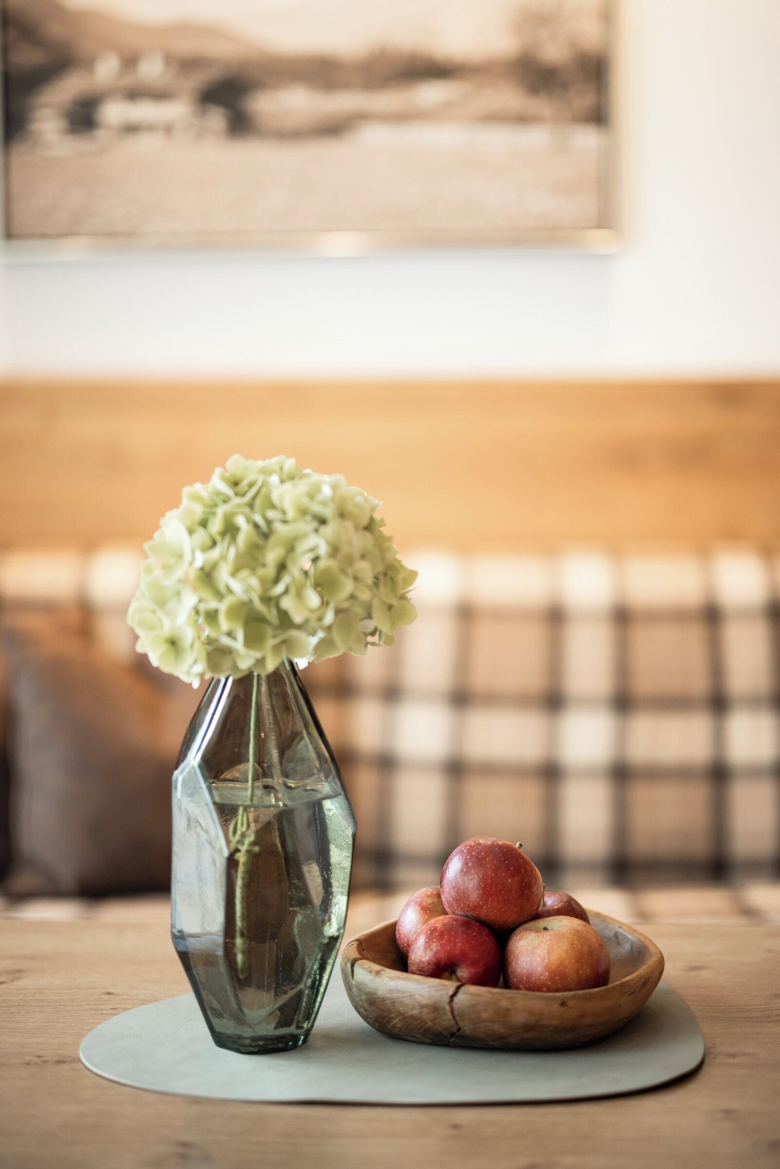 A table with a vase of flowers and a bowl of apples.