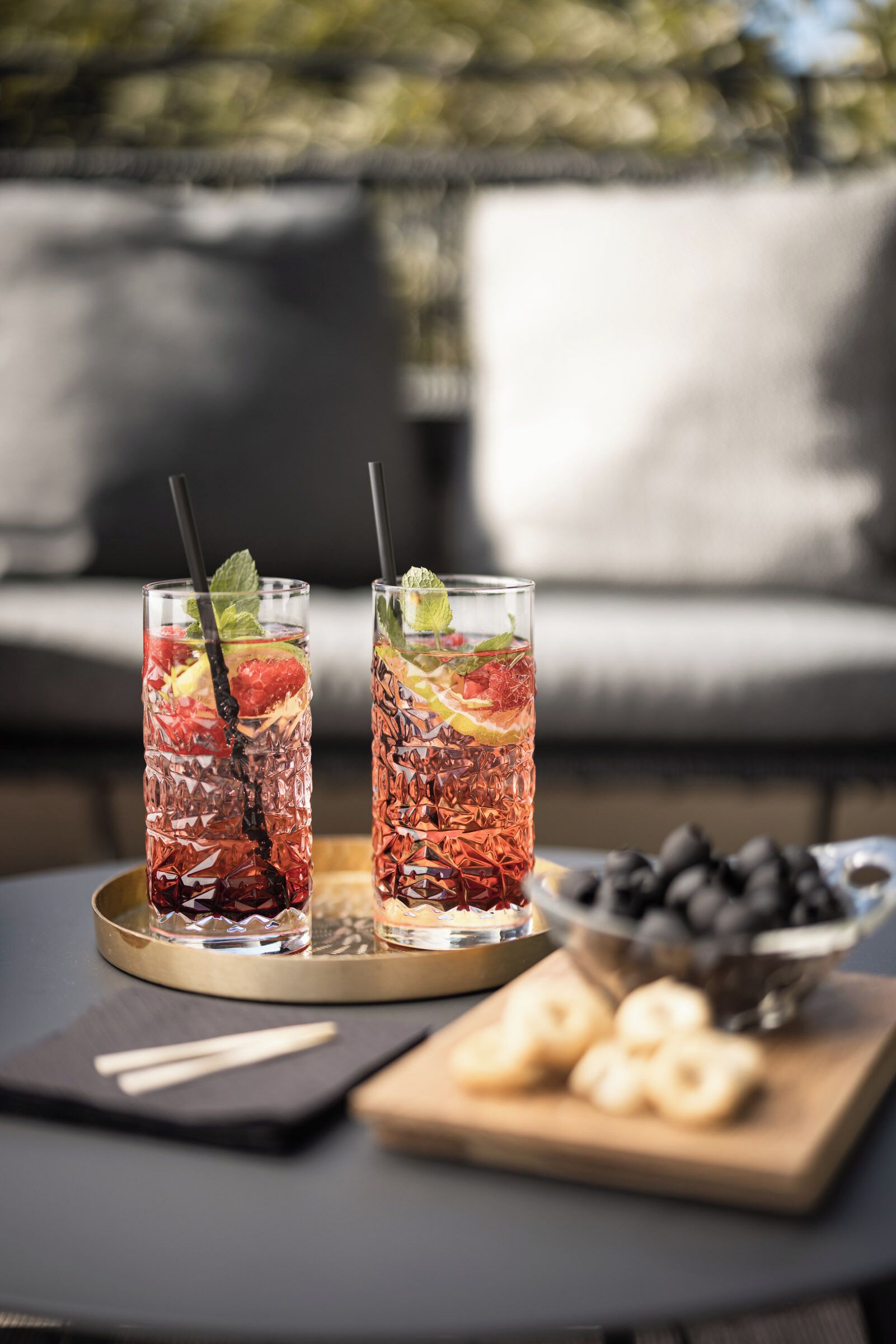 Two tall glasses of iced tea with fruit garnishes on a tray, a bowl of cookies, and a black napkin on a table.