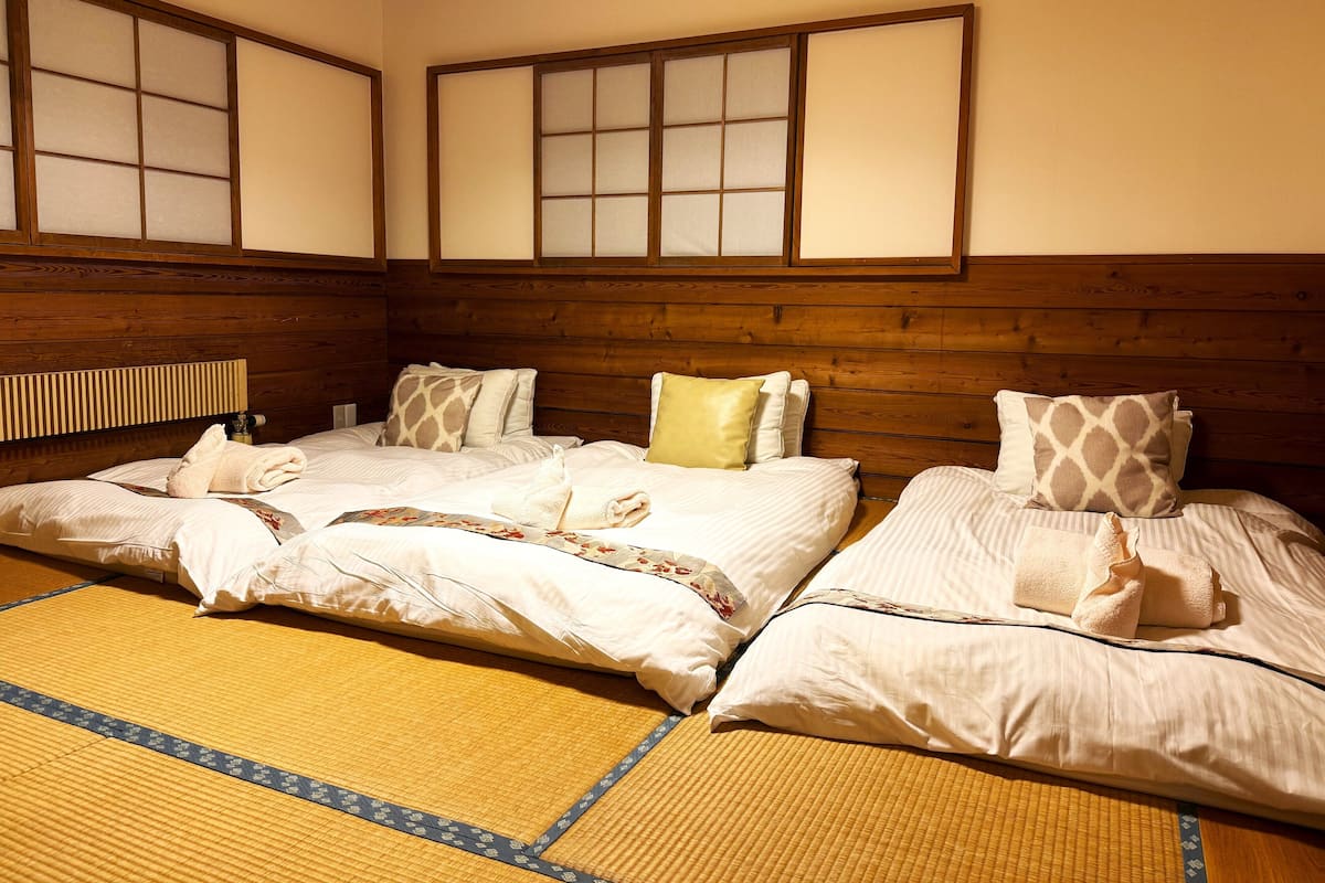 Quarto tradicional japonês com tatames, cabeceiras de madeira e biombos shoji.