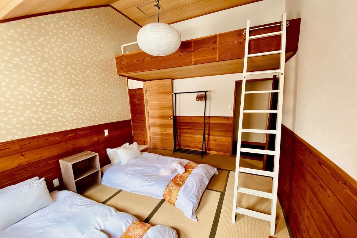 Quarto com duas camas, uma escada, luminária pendente e parede de madeira.
