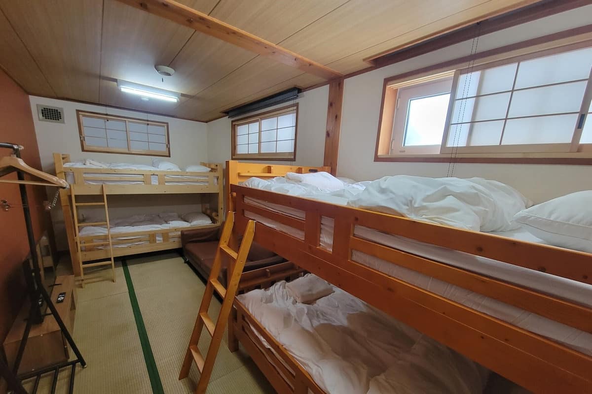 Um quarto de dormitório com beliches, um guarda-roupa de madeira e futons de tatame.