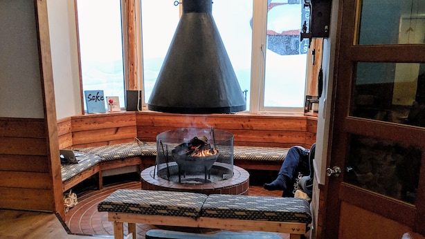 A cozy interior with a fireplace, seating area, and a view of the outdoors. - Raicho Lodge Madarao (Iiyama)