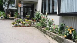 A building with a covered entrance, potted plants, and a sign indicating a business. - Stayful House Nakamachi (Hakuba)