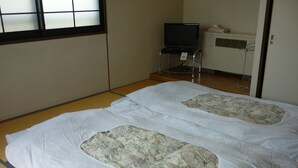 A room with tatami flooring, a futon bed with a floral-patterned mattress, a television on a stand, and a heater. - Stayful House Nakamachi (Hakuba)