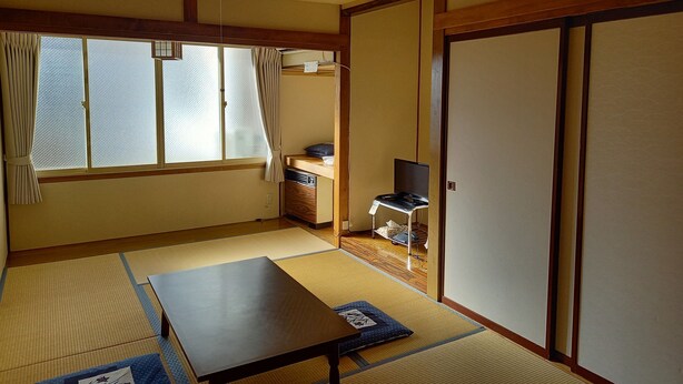 A traditional Japanese room with tatami flooring, a low table, a desk with a computer, and sliding doors. - Stayful House Nakamachi (Hakuba)