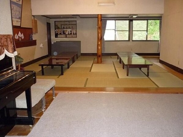 A traditional tatami mat room with a low table and benches, a wooden pillar, and a window with a view of greenery. - Stayful House Nakamachi (Hakuba)
