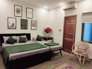 A bedroom with a double bed, a small bedside table with a vase, a chair, and a door. - Kon Tiki Hostel (Da Nang)