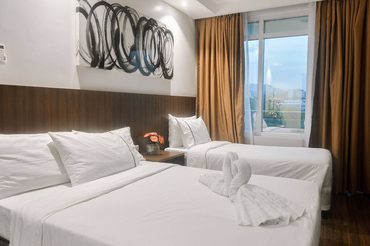 A hotel room with two beds, a large abstract painting, a vase with flowers, and a view of the city through the window.