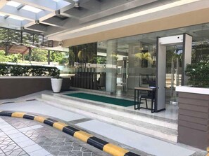 A modern building entrance with a glass door, a small outdoor seating area, and a green carpet leading to the entrance. - Home Solutions in Padgett Place (Cebu City)